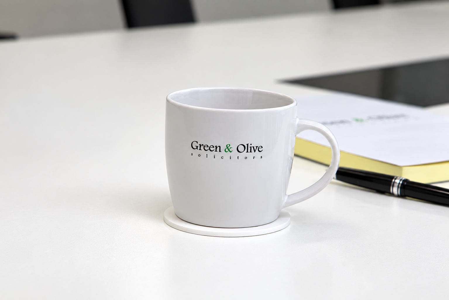 A Green & Olive branded mug and notepad on a meeting room table
